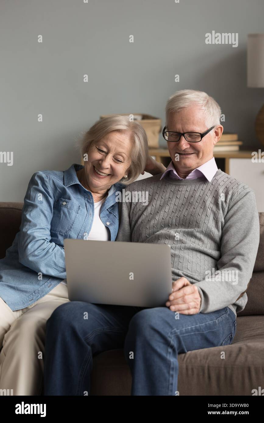 Happy mature spouses resting on sofa at home using laptop Stock Photo
