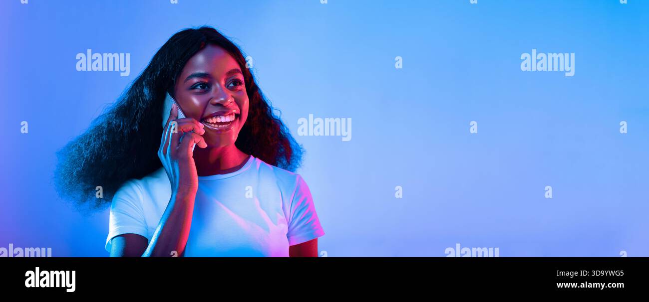 Young Woman Smiling While Talking on the Phone in Vibrant Lighting Stock Photo