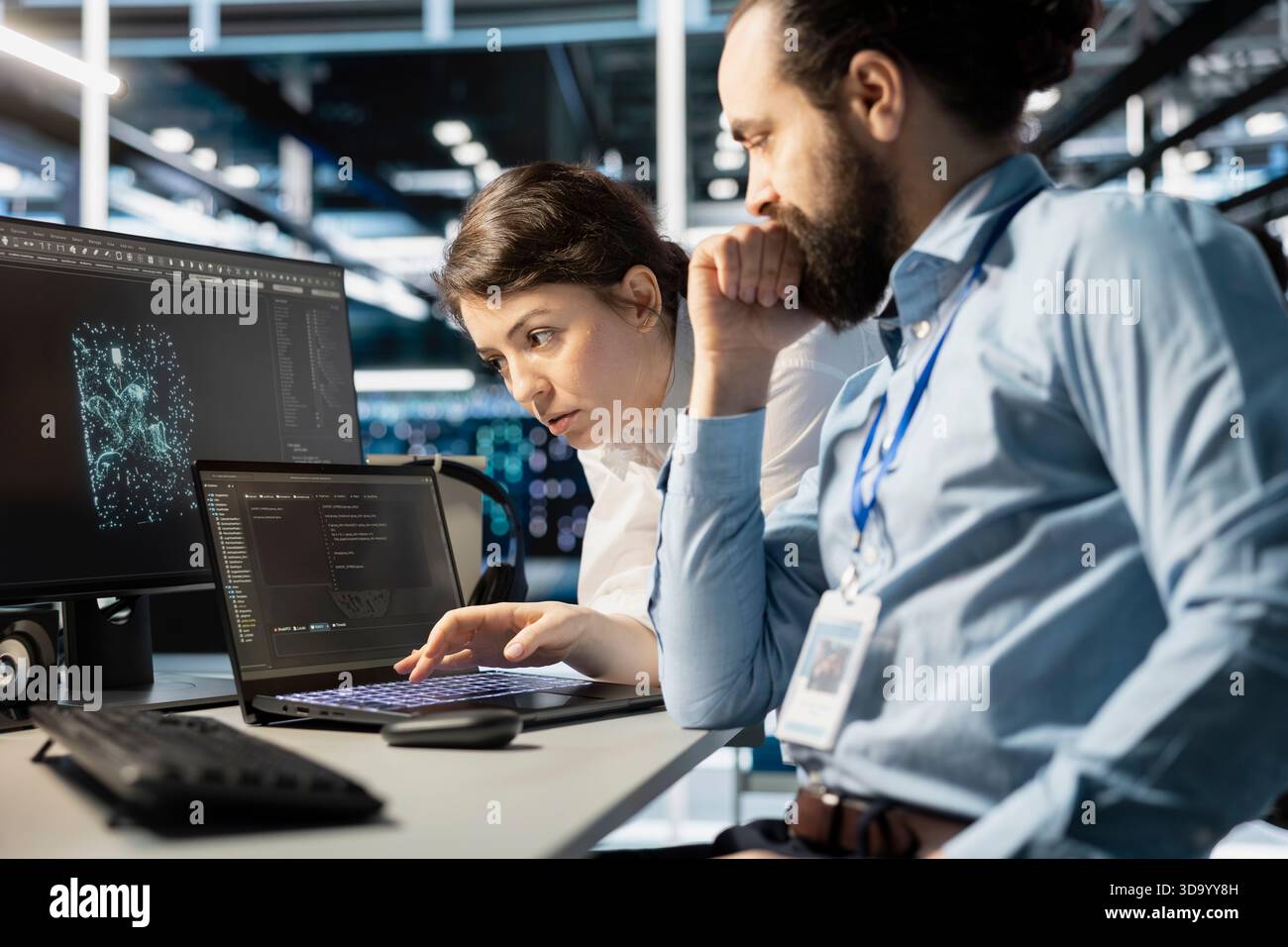 Team of programmers using notebook in server room, analyzing data. Data center office IT experts doing brainstorming, examining code on laptop, ensuring system integrity and security Stock Photo