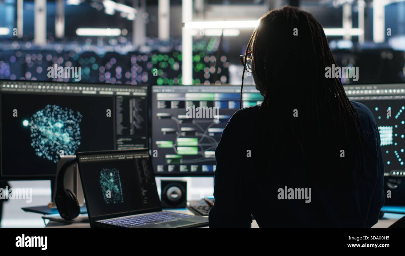 Data center programmer entering office uses node tree program to identify equipment performance issues. Server hub worker sitting at desk, reviewing data analysis graph to minimize failures, camera B Stock Photo