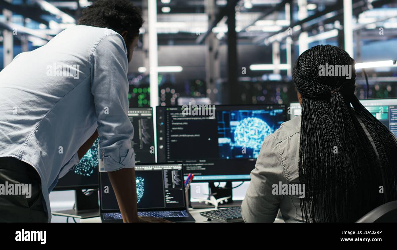 Data center manager supervising worker deploying AI solutions optimizing equipment. Server farm supervisor overseeing programmer using artificial intelligence to minimize systems downtime, camera B Stock Photo