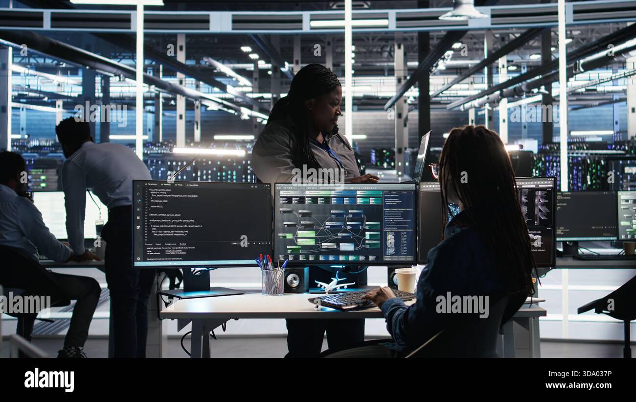 Data center manager supervising technician using node tree software to analyze datasets. Server room team leader oversees IT expert using visual programming tools to improve gear performance, camera A Stock Photo