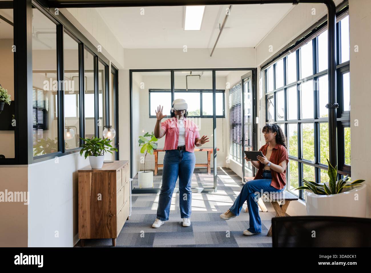 African American team demonstrating VR wearing white headset and pink top using tablet in office Stock Photo