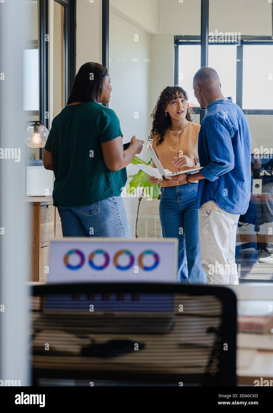 African American coworkers discussing plan while holding open laptop and phone in office bay Stock Photo