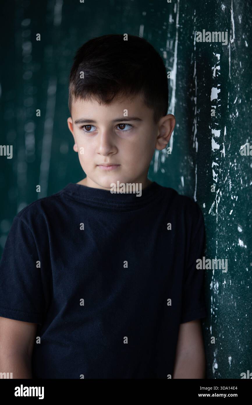 10 years old boy leaning against decayed wall looking away Stock Photo