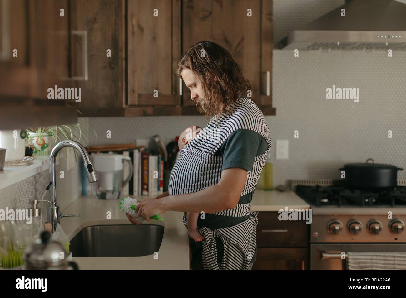 Stay at home dad babywearing and washing dishes Stock Photo