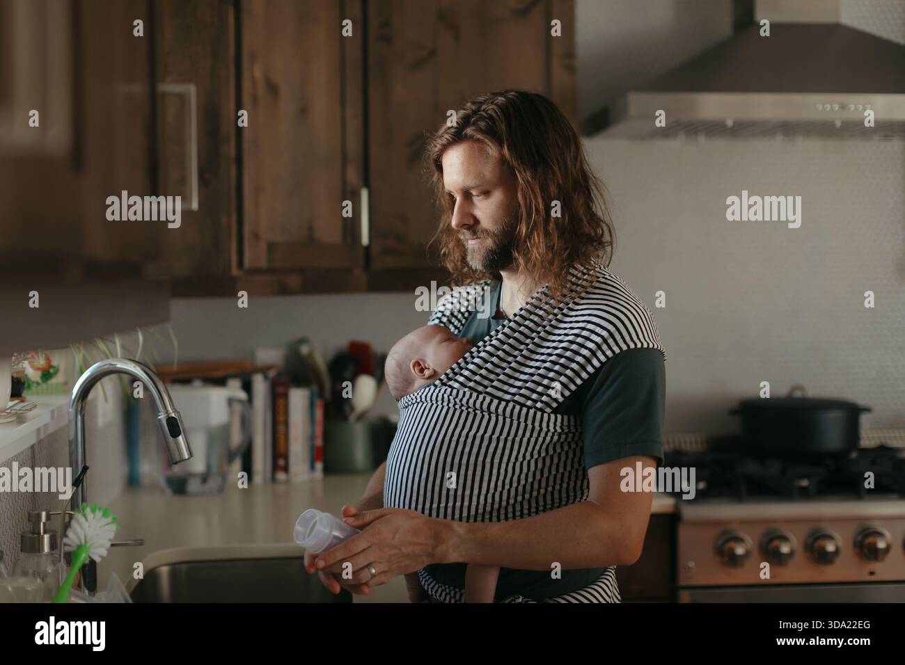 Stay at home dad babywearing by kitchen sink Stock Photo