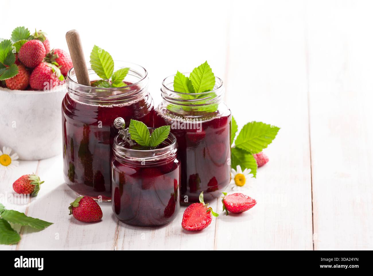 Three jars of strawberry jam with fresh strawberries on the table, close-up Stock Photo