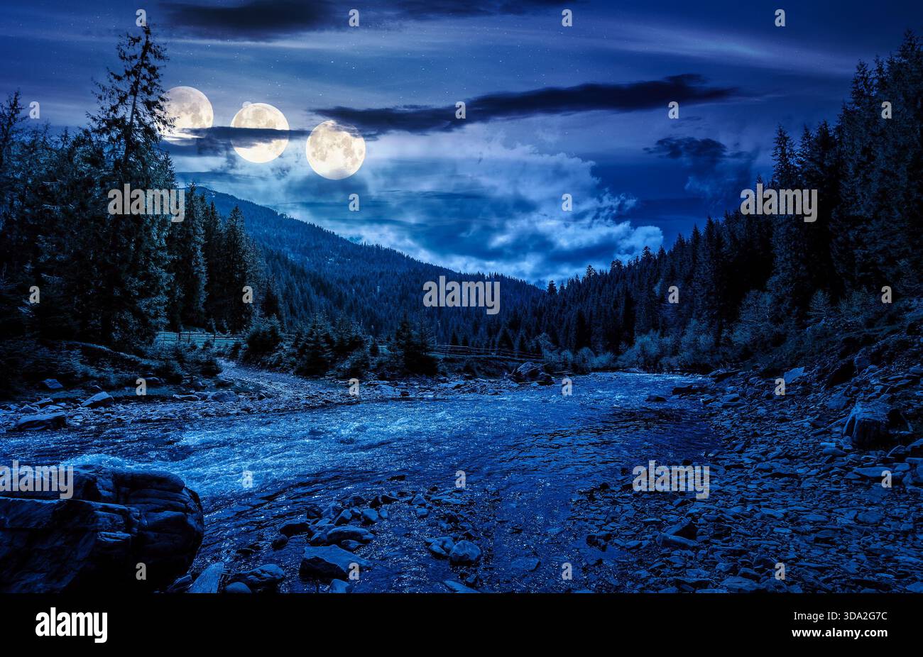 river flows through valley with forest at the foot of the mountain at night. scenic countryside in spring under cloudy sky in full moon light. backgro Stock Photo