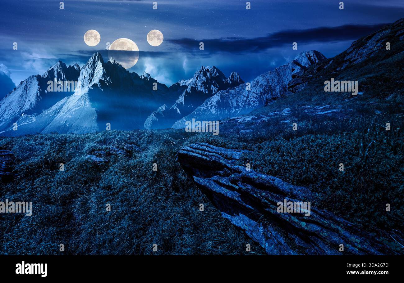 rocky peaks and rocks on hillside at night. scenic composite image of mountain landscape in summer in full moon light. rugged alpine scenery. backdrop Stock Photo