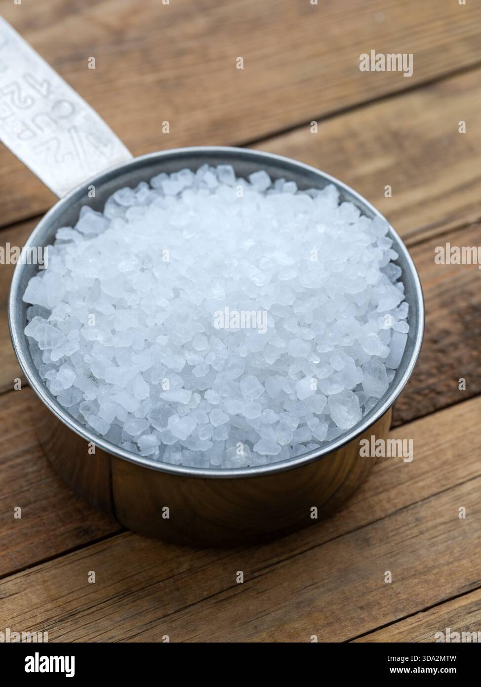 Coarse Sea Salt in Metal Measuring Cup on Wooden Surface Stock Photo