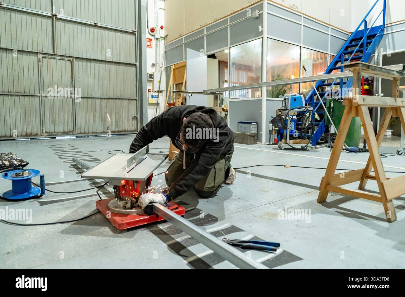 Worker operating a power tool, creating sparks while cutting a metal bar in a workshop Stock Photo