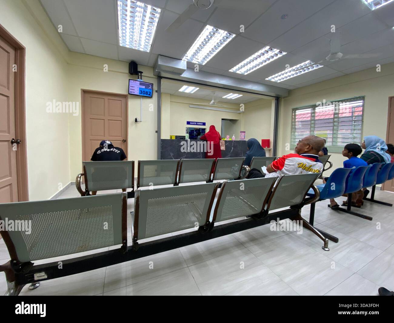 Waiting area in a government service office with numbered queue display, metal chairs, and counter for customer transactions. - Smartphone Captured Stock Image
