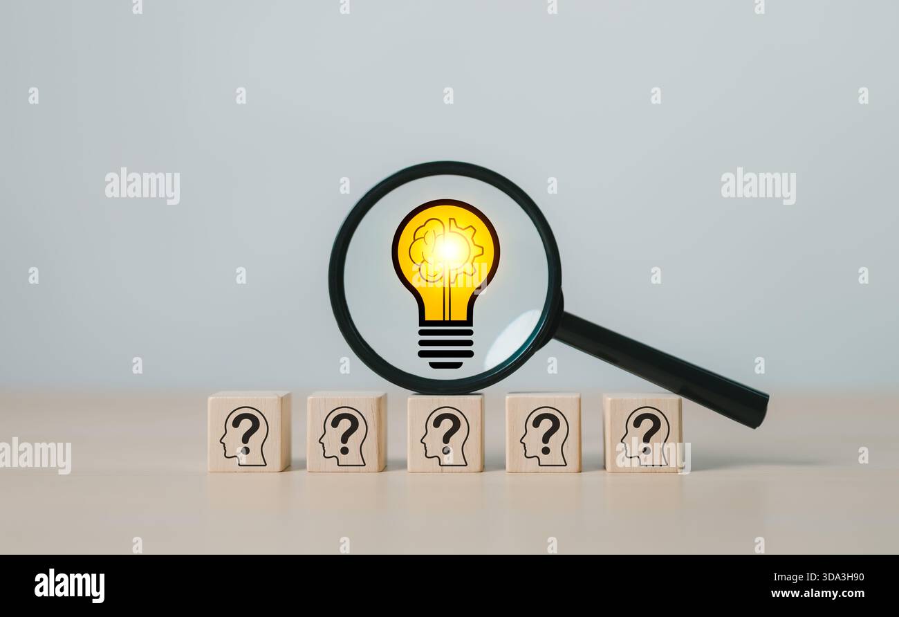 Innovation and Problem Solving Concept. Magnifying glass focuses on light bulb icon above wooden blocks with question marks, creative solutions, Stock Photo