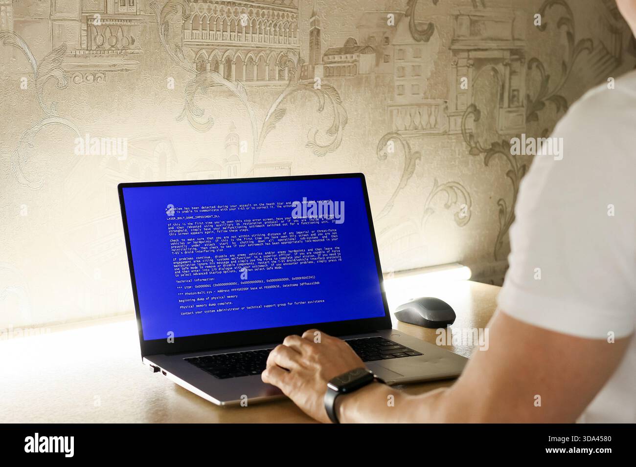 Individual working at desk with computer displaying system failure message on blue background Stock Photo