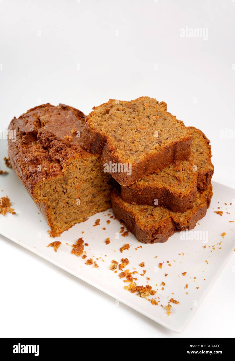 Homemade carrot bread loaf with several sliced pieces and crumbs on a white rectangular plate Stock Photo