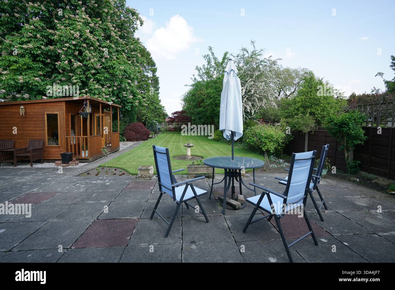 Seating area with table and chairs in garden with shed and pathway during daytime Stock Photo