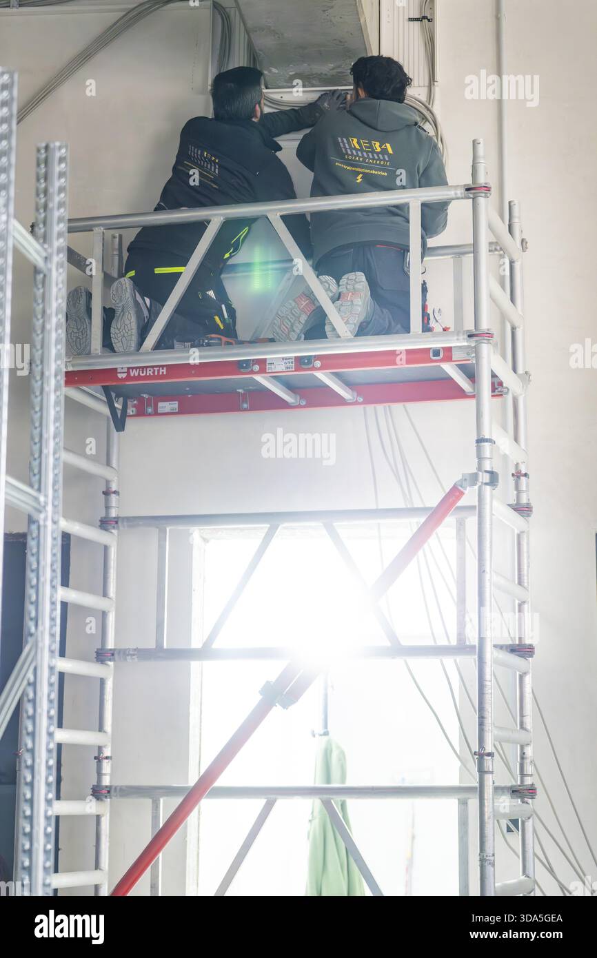 Two workers standing on scaffolding and working on a ceiling with strong light, electrician, new building, Germany Stock Photo
