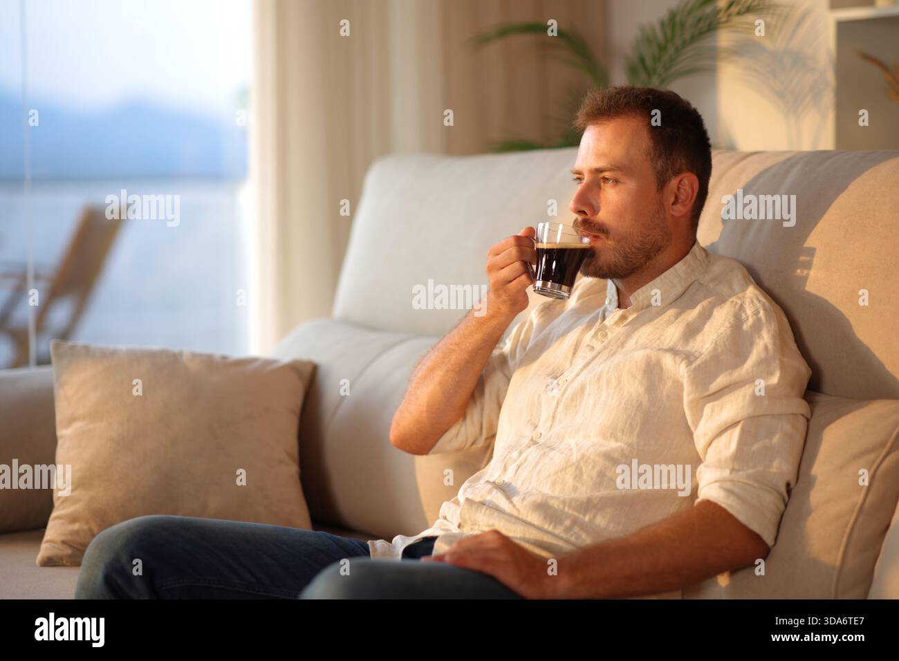 Man drinking coffee alone at sunset sitting on a sofa at home Stock Photo