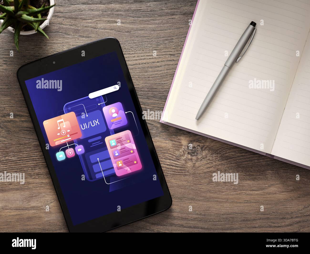 Tablet showing app development and user interface design elements on a wooden workspace with a notebook and pen Stock Photo