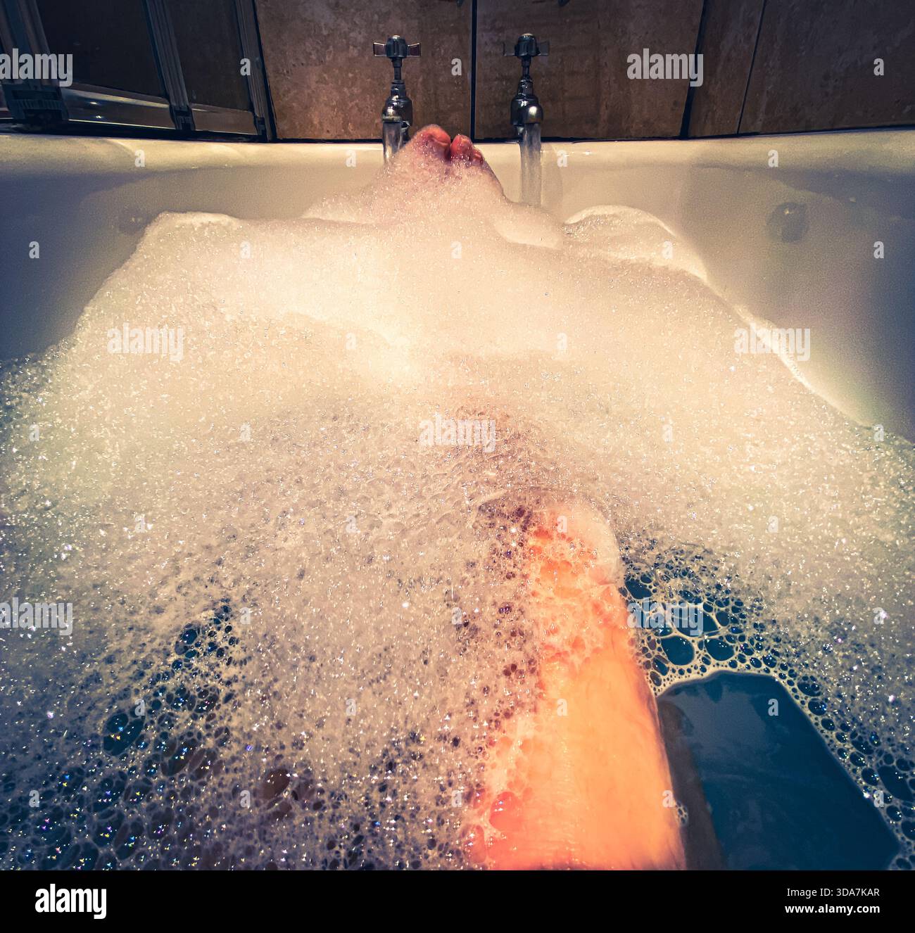 Womens legs seen through bubbles a she relaxes in a bath - Smartphone Captured Stock Image