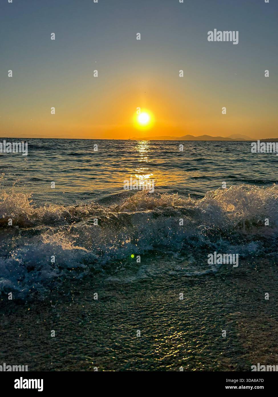 A vibrant golden sunset reflects over calm sea waves as they break softly on the shore, capturing a peaceful seaside moment full of warm light and mot - Smartphone Captured Stock Image