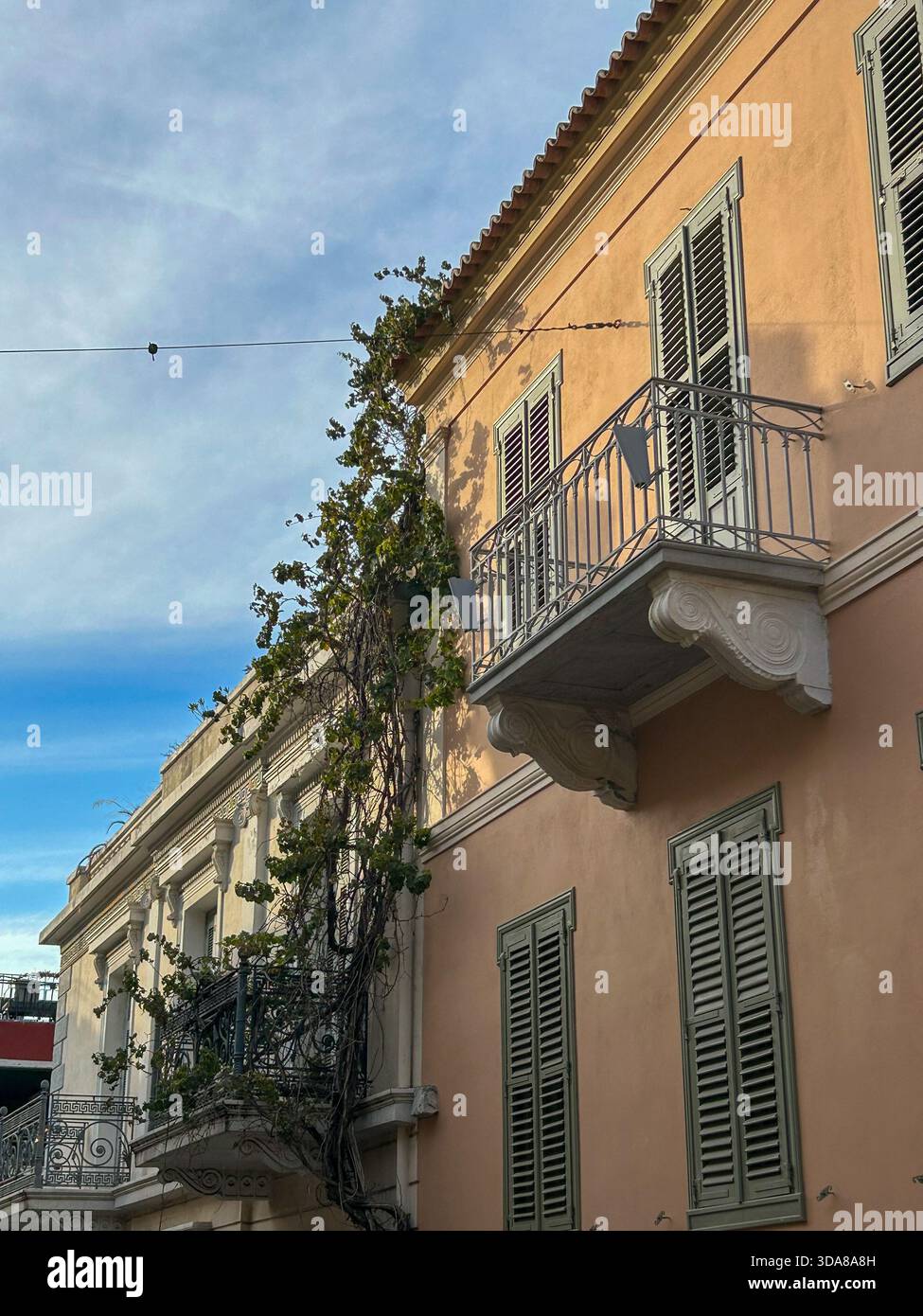 A neoclassical Athens building with peach walls, green shutters, wrought-iron balconies, and climbing vines illuminated by warm afternoon light. - Smartphone Captured Stock Image