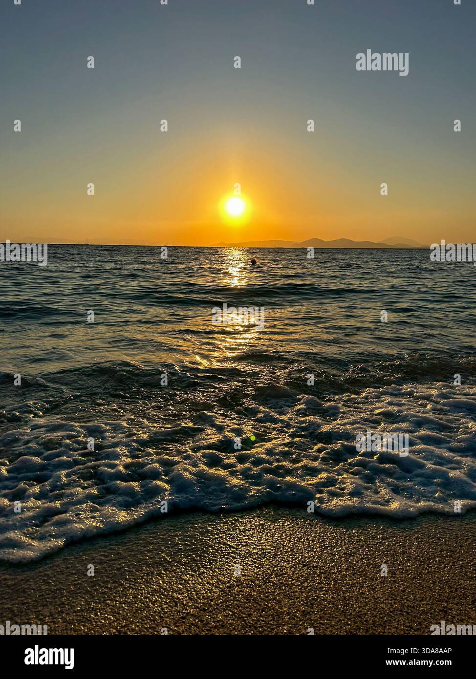 Golden sunset over the ocean with gentle waves and warm colors reflecting across the water and sandy shore. - Smartphone Captured Stock Image