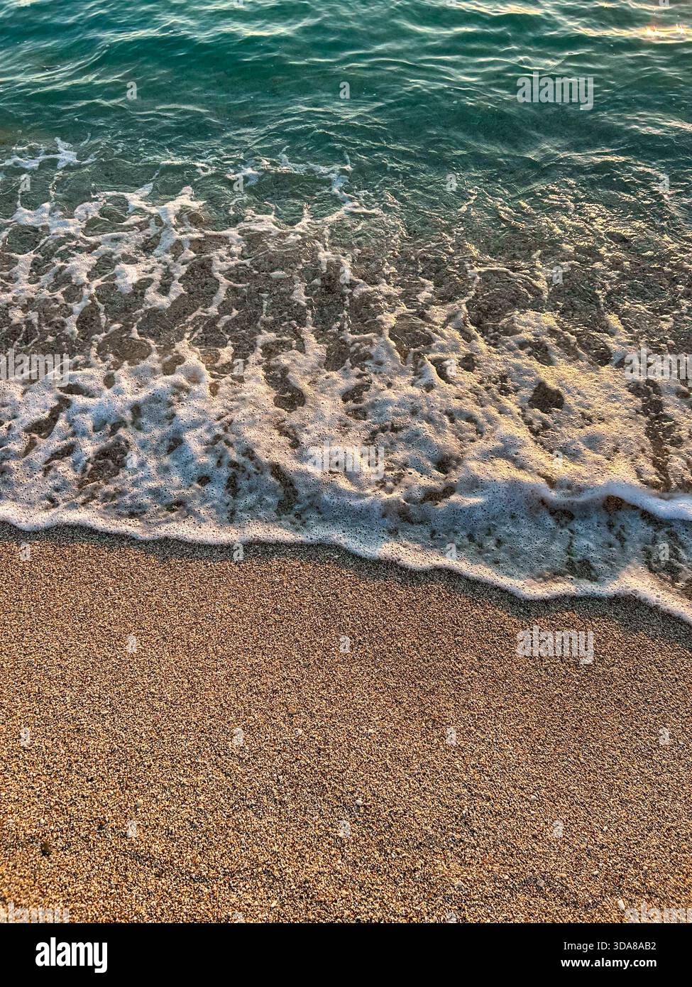 Clear turquoise waves gently recede over a pebbly beach, creating white foam patterns and revealing the natural texture of small, colorful stones. - Smartphone Captured Stock Image