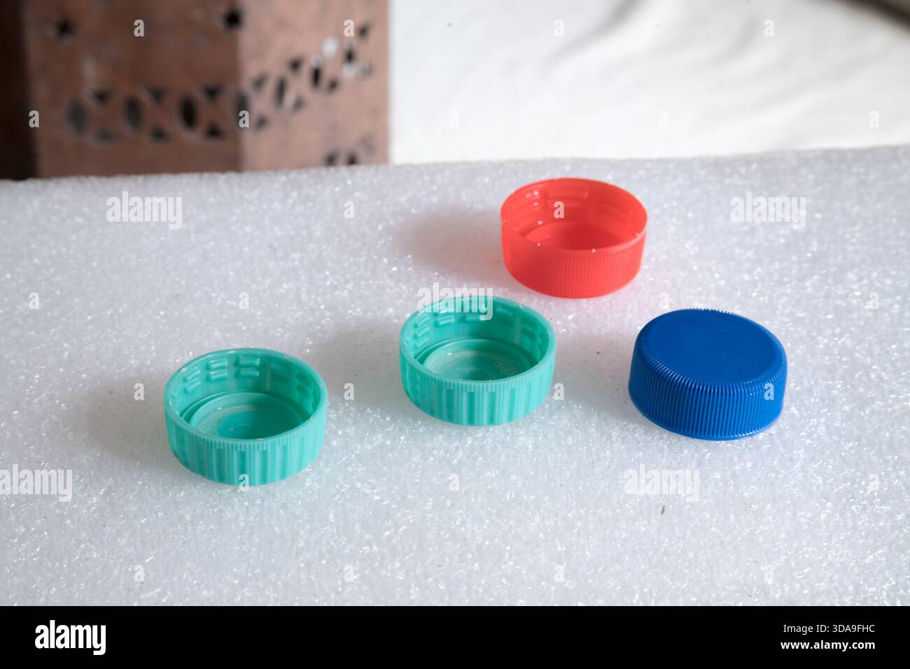 four plastic bottle caps on a bumpy white surface in the foreground Stock Photo