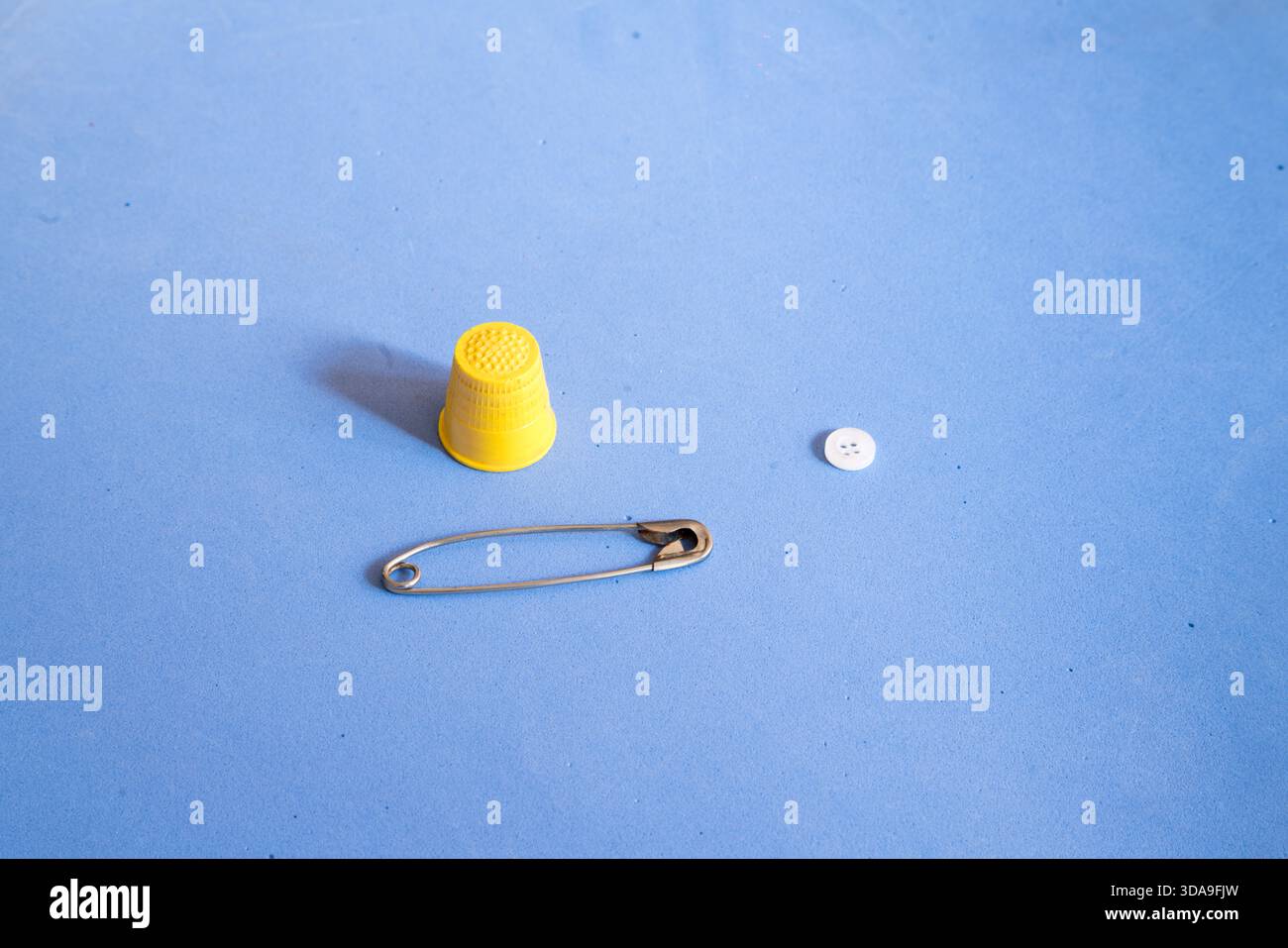 a safety pin, a thimble, and a button on a blue textured surface. Stock Photo