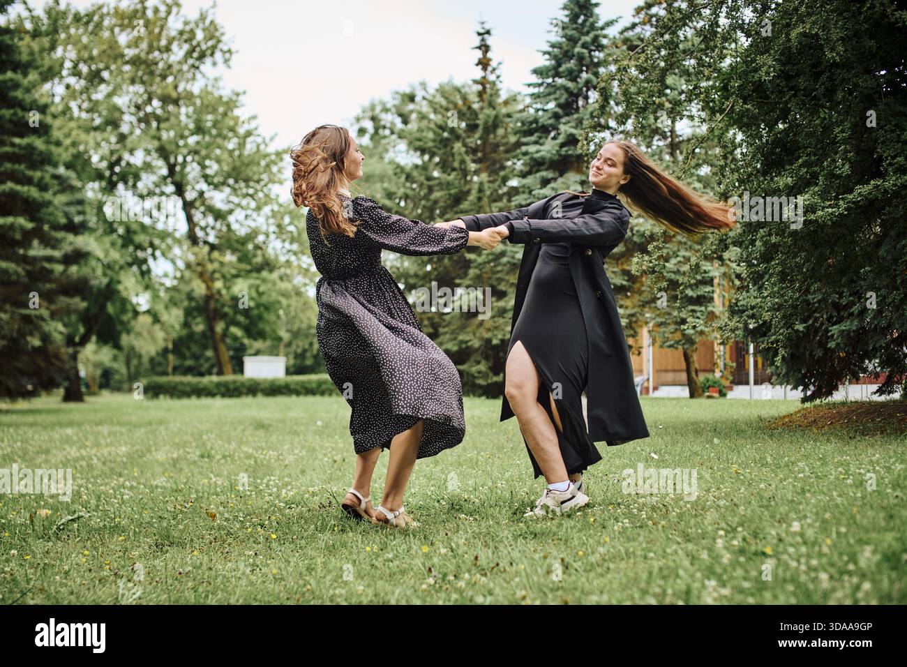 Two young women wearing black dresses spin joyfully while holding hands ...
