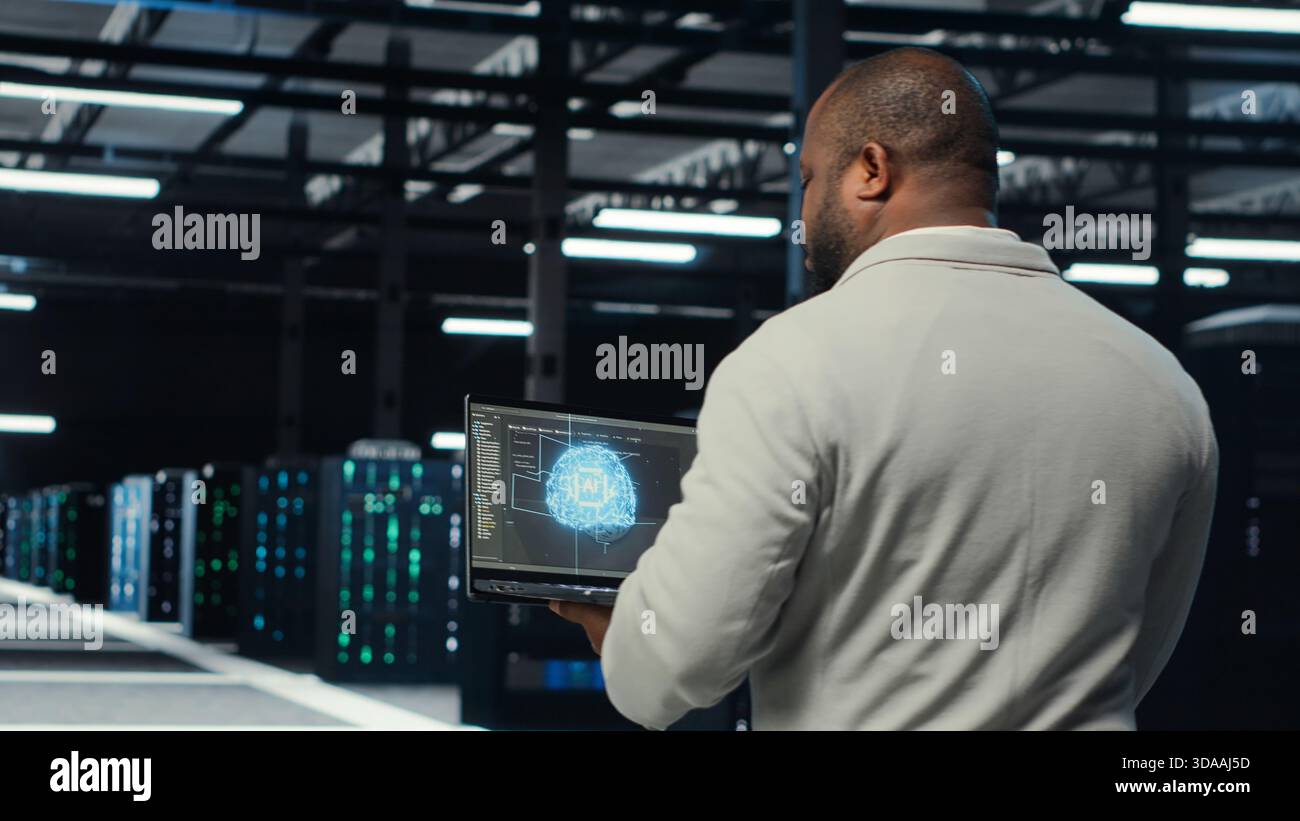Technician using laptop in data center, managing server virtualization, running scripts. IT expert using programming language on notebook in server hub, finetuning network protocols, camera B Stock Photo