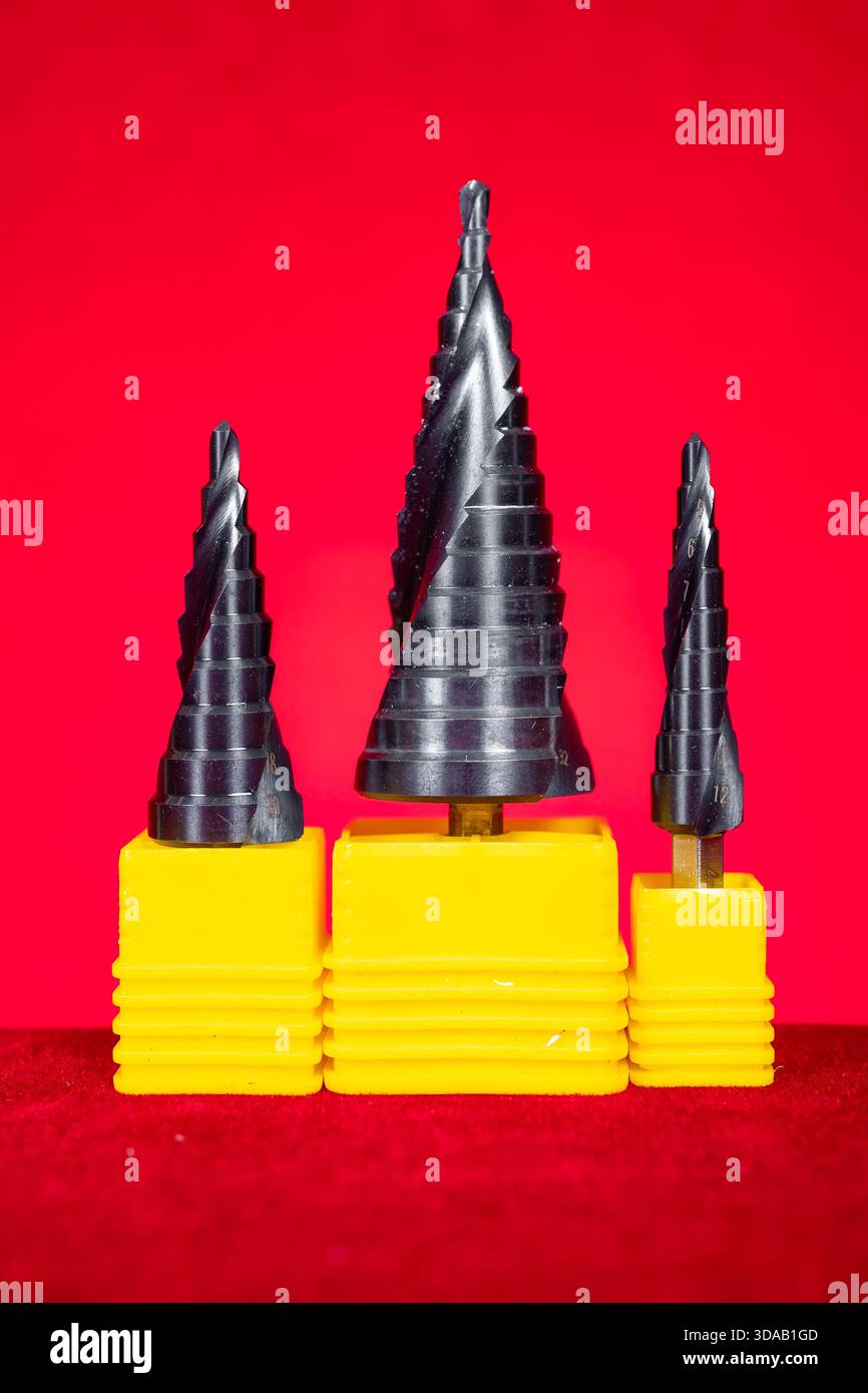 a set of conical step drill bits in various sizes on red at vertical composition Stock Photo