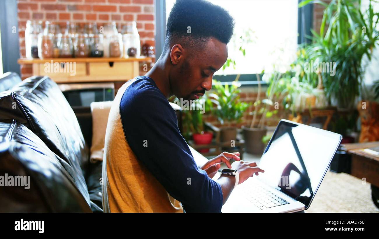 Man is checking smartwatch while working on laptop on sofa in flat design loft, technology theme Stock Photo