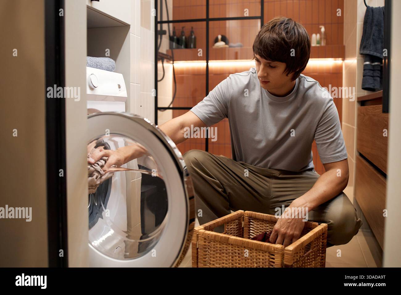 Young Man Loading Laundry into Washing Machine in Modern Bathroom Stock Photo