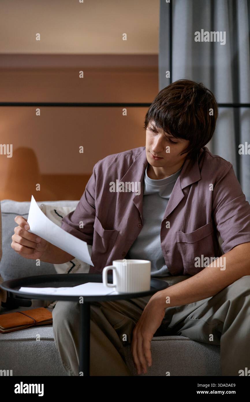 Young Man Reviewing Documents While Sitting Indoors on Sofa Stock Photo