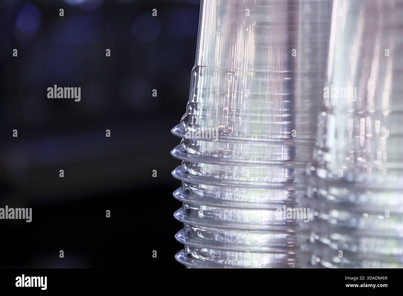 Close up detail of stack of clear transparent plastic disposable cups with repeating pattern. empty drinkware items sit organized against dark backgro Stock Photo