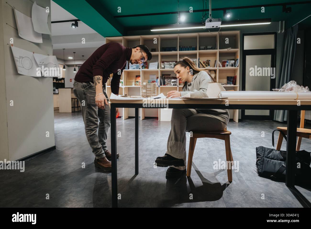 Two students collaborate at a design studio table, reviewing plans in a modern collaboration center. Stock Photo