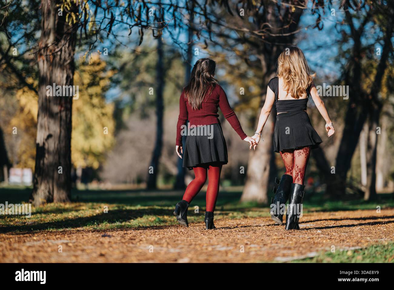 Two women walking hand in hand in a park during autumn, showcasing ...
