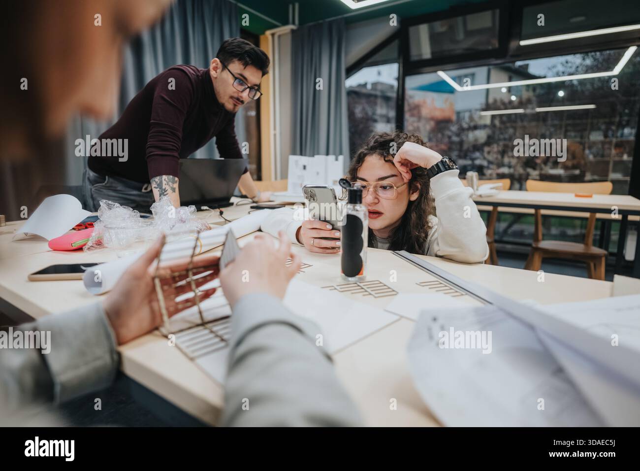 Students collaborate at a workshop table, using laptops and phones during a group study session Stock Photo