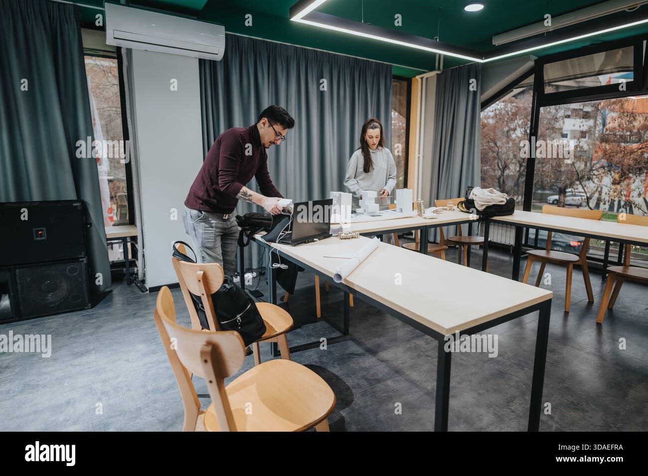 Two students collaborate in a modern classroom workshop space with laptops and materials on a long table Stock Photo