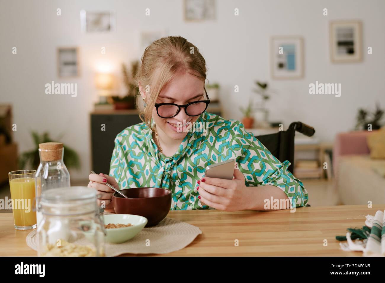 Young Woman with Disability Smiling While Using Smartphone at Breakfast Stock Photo