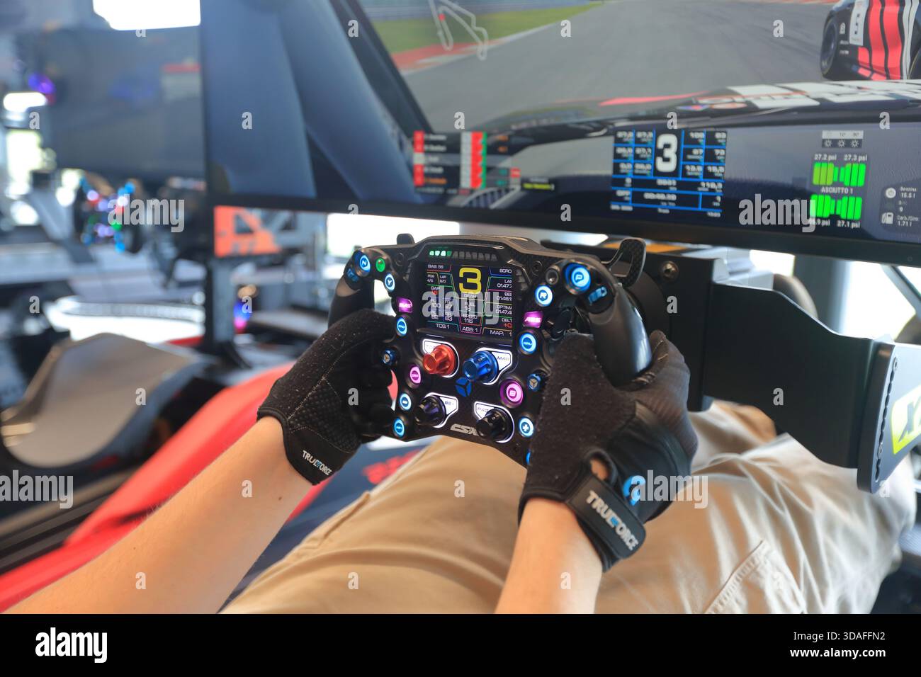 Players participate in a race in the racing car driving simulator at the Marco Simoncelli World Circuit. Detail of the driving steering wheel. - Stock Image