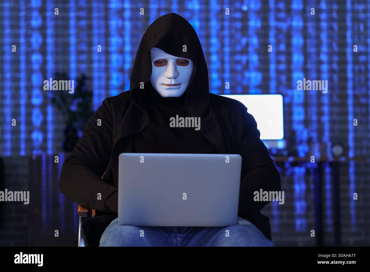 Hacker with laptop sitting in dark room Stock Photo