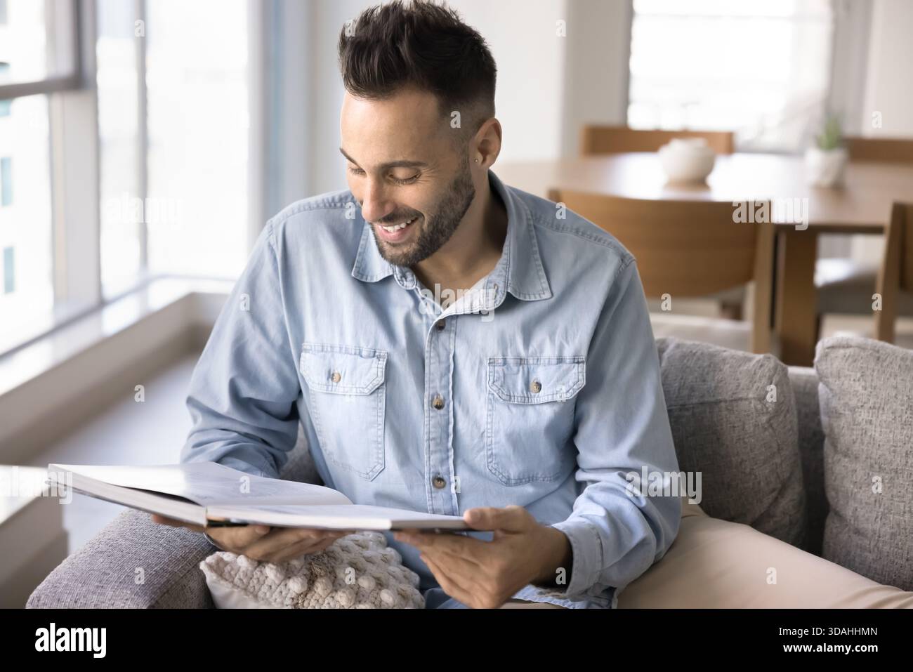 Smiling Hispanic man reading book while relaxing at home Stock Photo