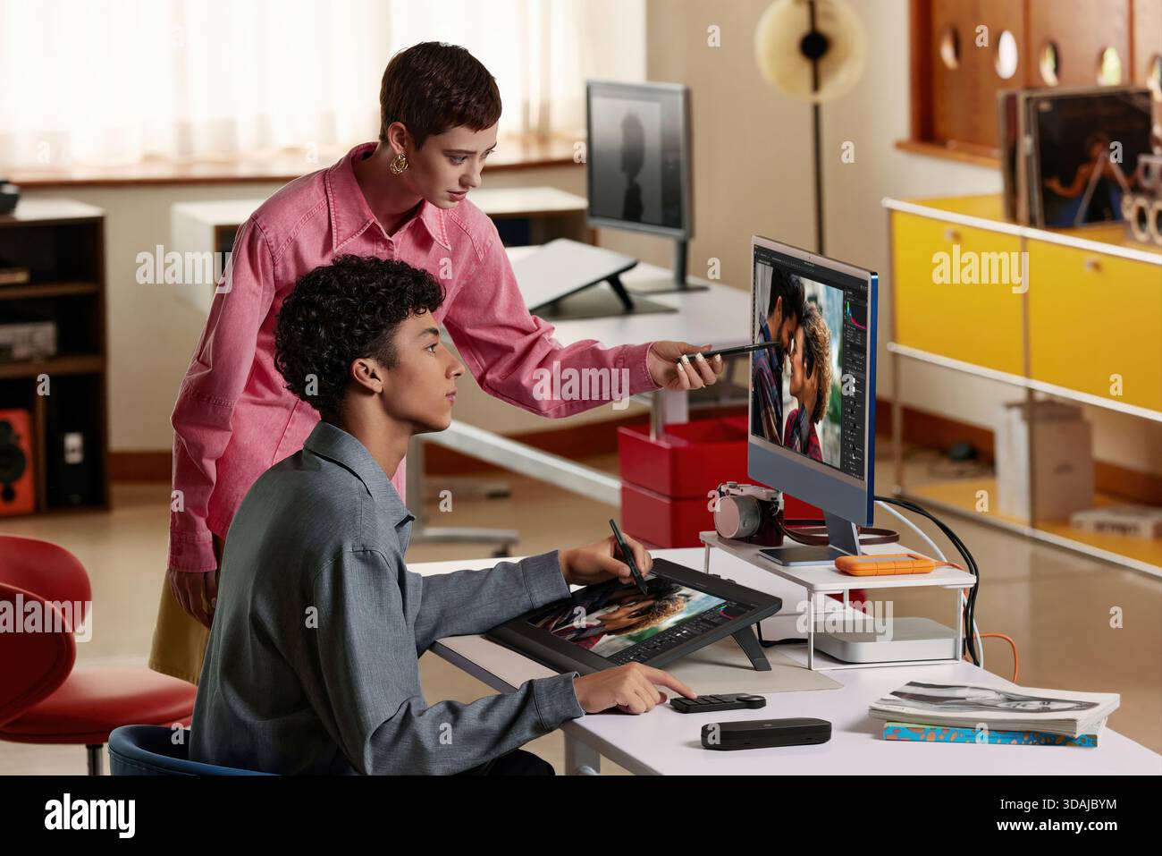 Two creative professionals collaborating and discussing image editing project on computer screen using graphics tablet Stock Photo