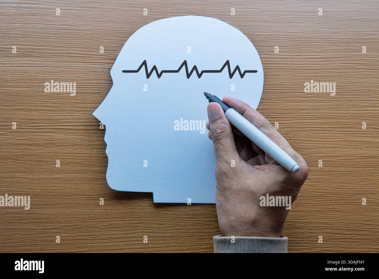 A hand drawing a brainwave line on a paper cutout of a human head ...