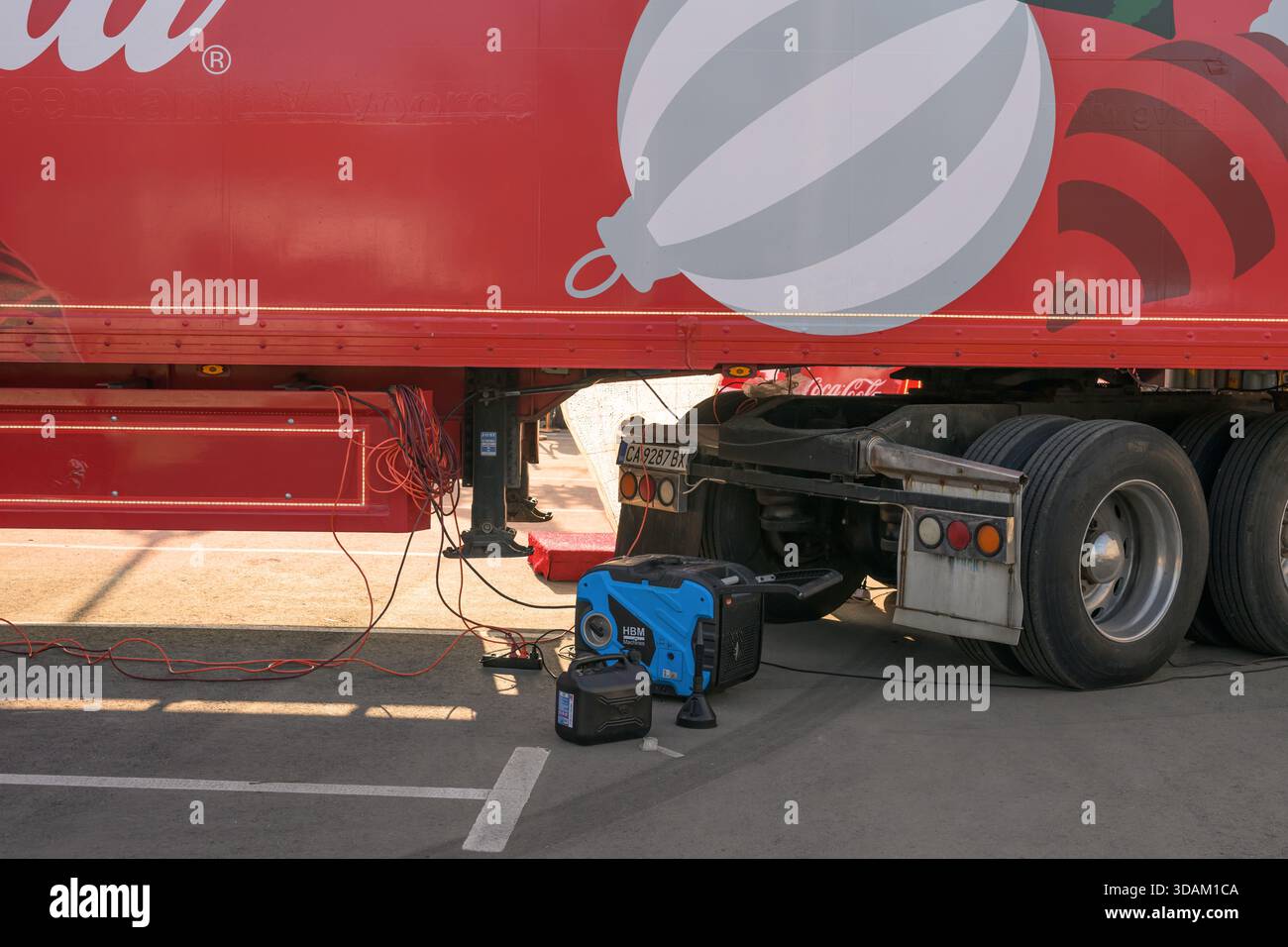 12/11/2025 - Ruse, Bulgaria:A generator and fuel can sit beneath the Coca-Cola Christmas truck trailer with cables running toward the vehicle in Ruse, Bulgaria. Stock Photo