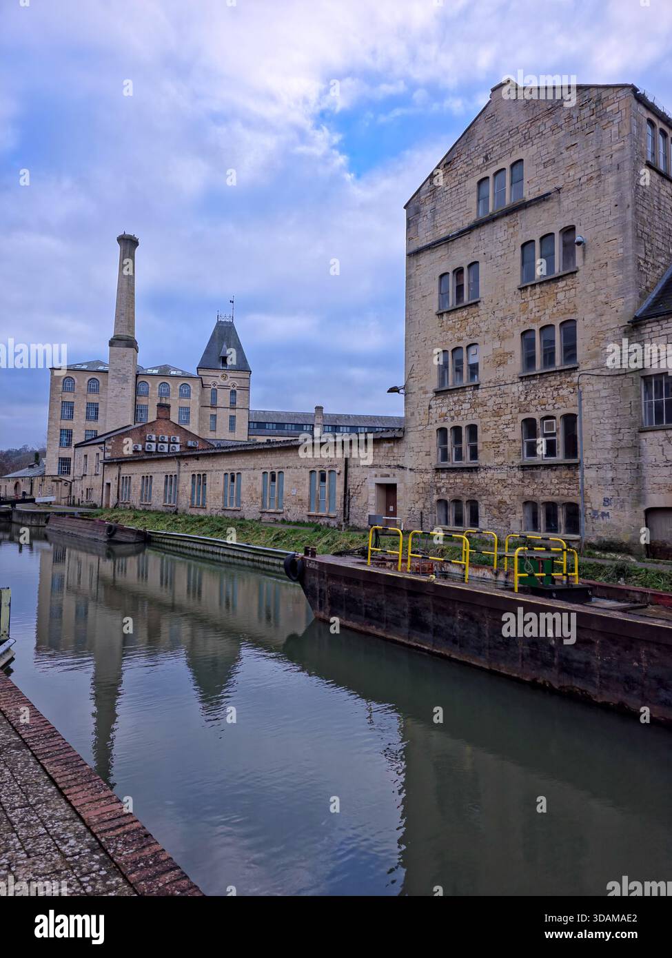Historic Ebley Mill (Stroud Mill) with tall chimney and canal-side industrial buildings reflected in the calm Stroudwater Canal on a winter day, - Smartphone Captured Stock Image